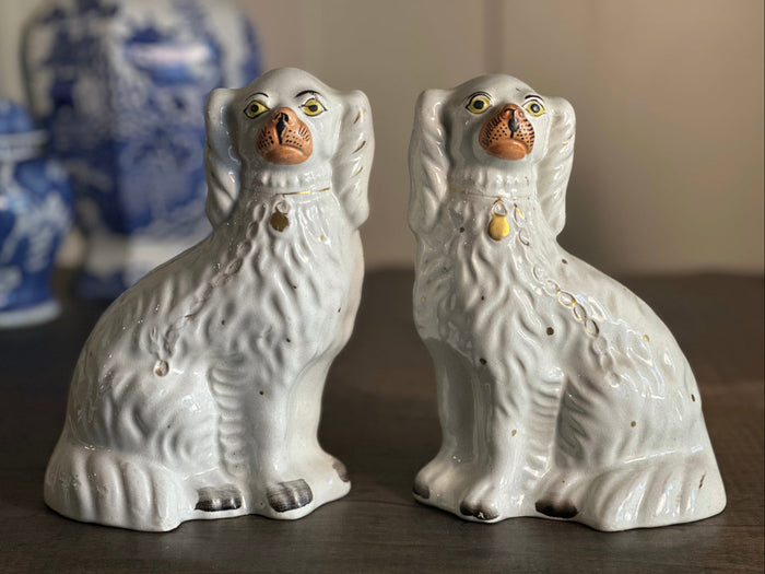 Pair of brown and white facing Staffordshire pottery spaniels on a mantle in front of an oil painting