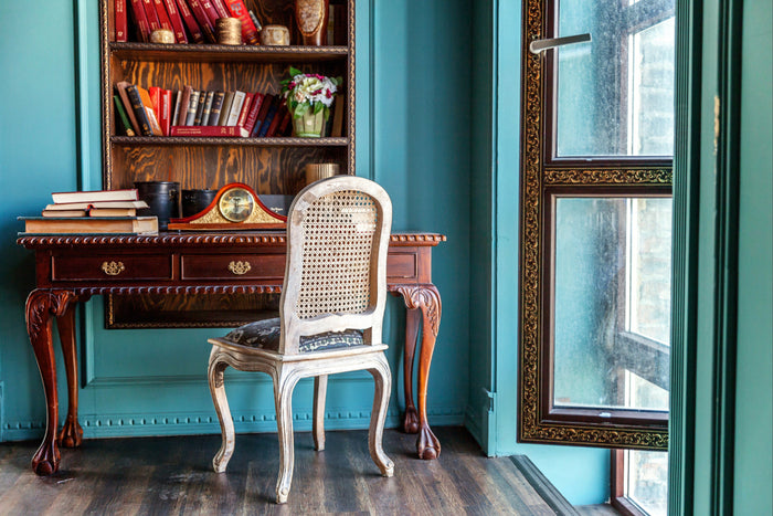 Eclectic modern living room featuring a navy blue gallery wall, vintage artwork, leopard print chairs, and a Persian rug layered with books.