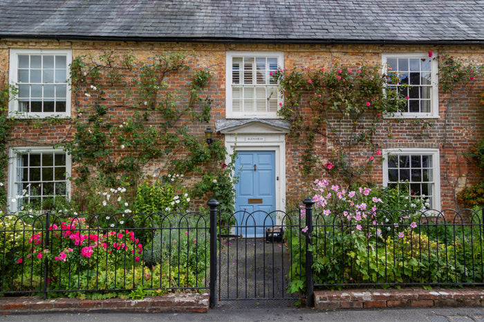 Charming honey-stone cottage in the Cotswolds with a slate roof, lush garden, and weathered stone wall with wooden gate in the foreground.