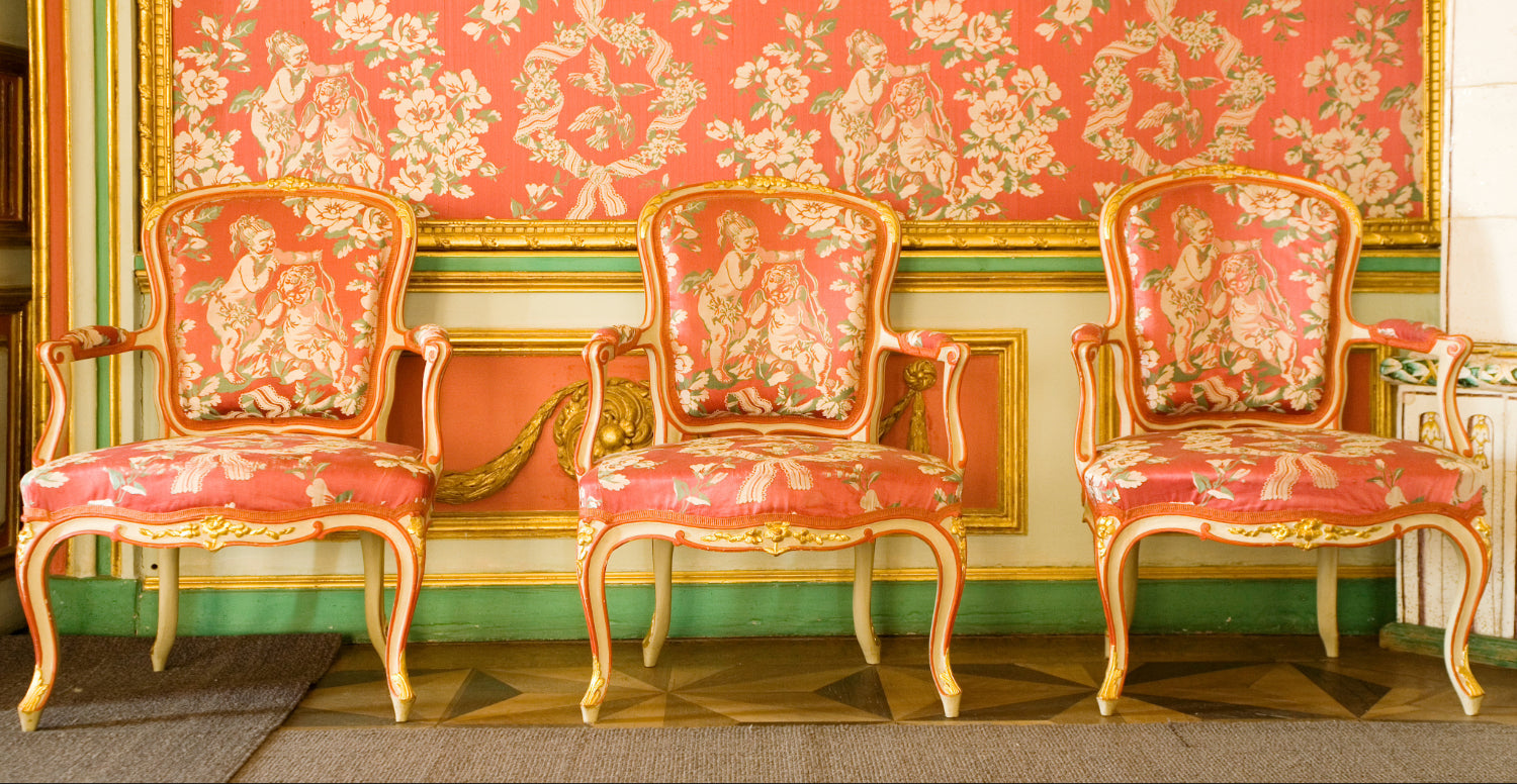 Traditional English country drawing room with green panelled walls, gilded portraits, antique fireplace, and layered textiles.
