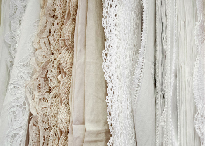 Flat lay of antique Irish lace samples on blue textile background, featuring floral and butterfly motifs, needle lace, and Victorian-era lace designs.