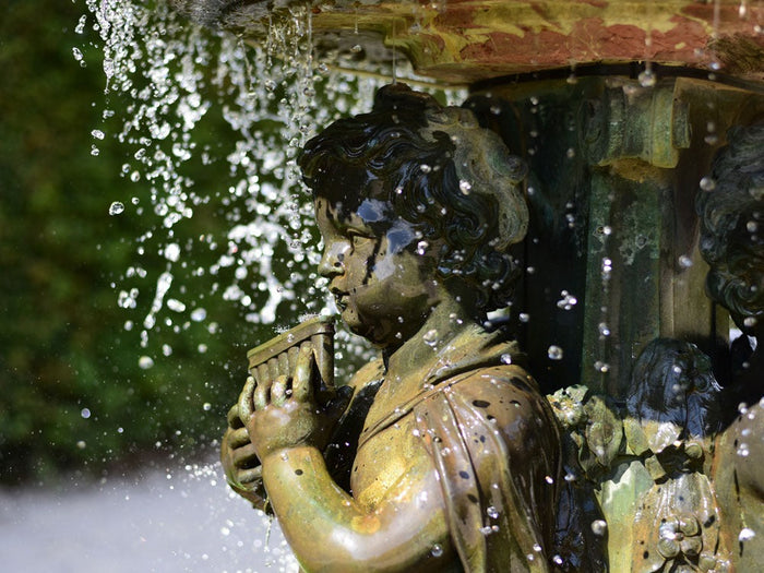closeup of stone cherub boy in fountain with water pouring over him from the upper basin