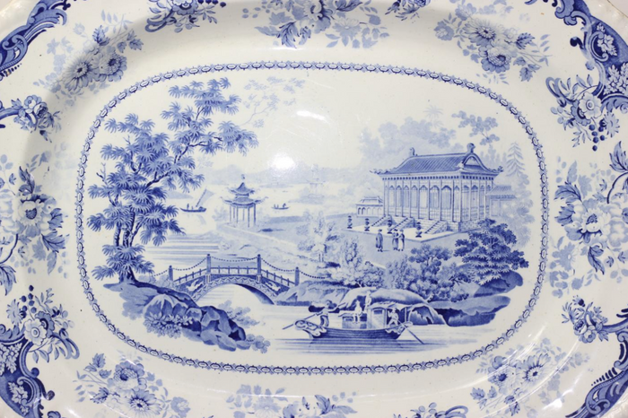 Close up of blue and white transferware platter depicting chinoiserie scene and classical botanical motif around the border