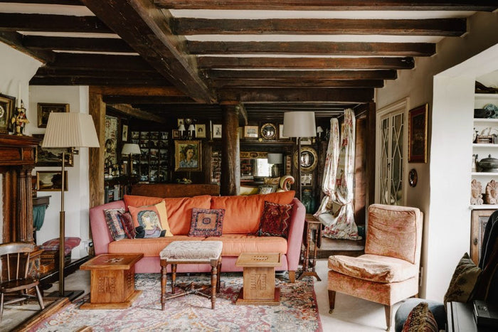 Cozy English country living room with heritage interiors, featuring exposed beams, vintage textiles, eclectic artwork, and antique furniture.