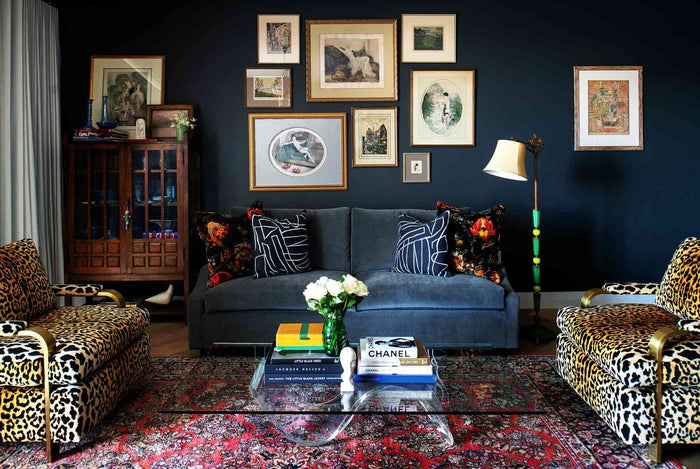Eclectic modern living room featuring a navy blue gallery wall, vintage artwork, leopard print chairs, and a Persian rug layered with books.