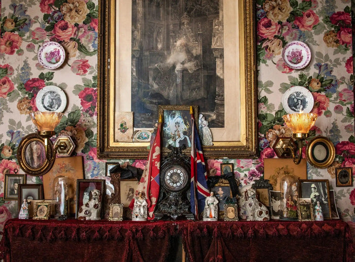 Victorian mantel display with floral wallpaper, framed portraits, Staffordshire figurines, and Union Jack flags.