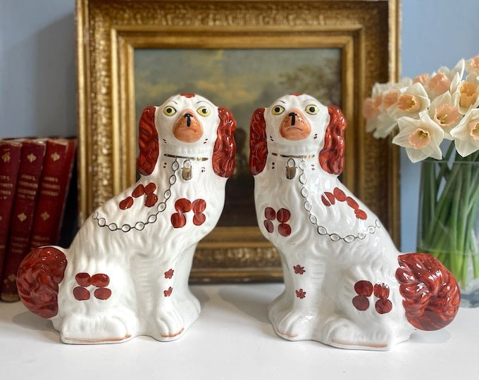 Pair of brown and white facing Staffordshire pottery spaniels on a mantle in front of an oil painting