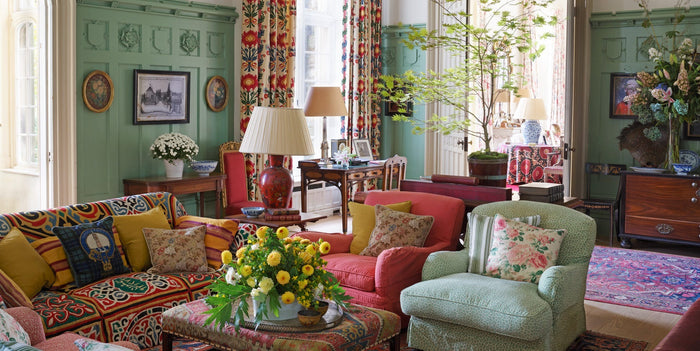 English country sitting room with red and pale blue furniture and accents, yellow flowers on the table in the center, and floral motifi curtains